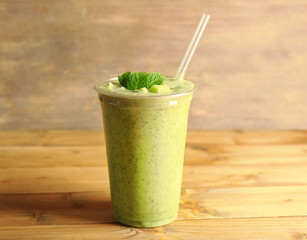Delicious kiwi milkshake in plastic cup on wooden background