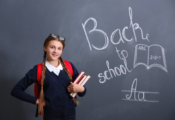 Girl with backpack and books standing near school blackboard