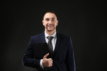 Young business coach with clipboard standing on black background