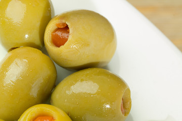 White plate of green olives filled with red paprika standing at wooden table background.