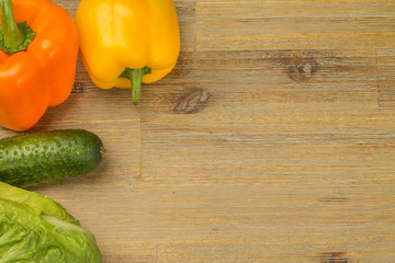 Vegetables on wooden table background around the sides. Cucumbers, greens, cutting board, bell peppers orange and yellow. Vegan or vegetarian. Healthy eating. Salad.