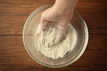 Female hand and glass bowl with flour on kitchen table, close up