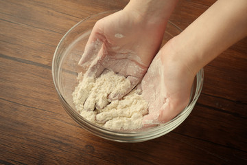 Female hands and glass bowl with flour on kitchen table, close up