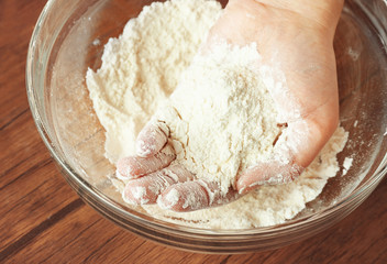 Female hand and glass bowl with flour on kitchen table, close up