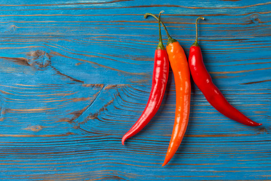 Three chili peppers on blue wooden background