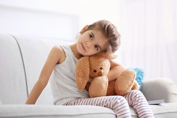 Funny little girl with cuddly toy sitting on sofa at home