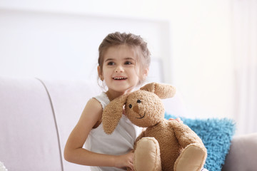 Funny little girl with cuddly toy sitting on sofa at home