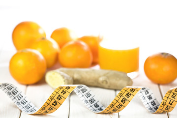 Measure tape with ginger, oranges and juice blurred on wooden wh