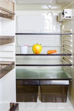 A yellow apple, a carrot eun yogurt container on a shelf in a refrigerator