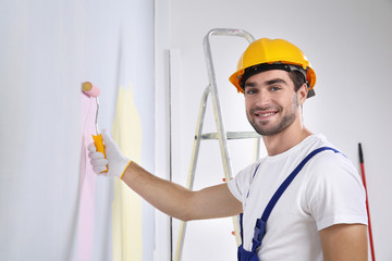 Young worker painting wall in room