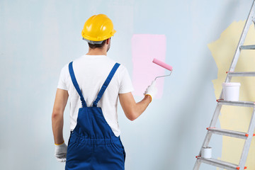 Young worker painting wall in room