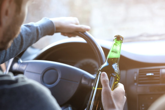 Man holding bottle of beer while driving car, closeup. Don't drink and drive concept