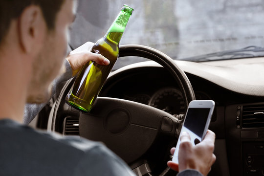 Man holding mobile phone and bottle of beer while driving car, closeup. Don't drink and drive concept