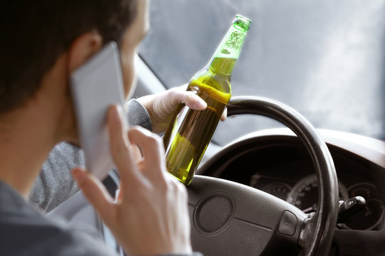 Man talking by mobile phone and holding bottle of beer while driving car, closeup. Don't drink and drive concept