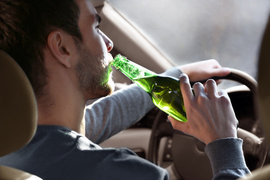 Man drinking beer while driving car, closeup. Don't drink and drive concept