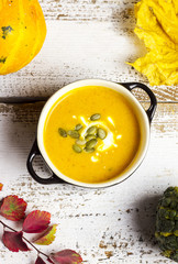 creamy pumpkin soup on a rustic white background with autumn lea