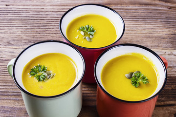 Pumpkin soup in enamel mugs, with pumpkin seeds and parsley