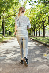 Fototapeta premium Back view of running woman in the park. Autumn weather, yellow foliage