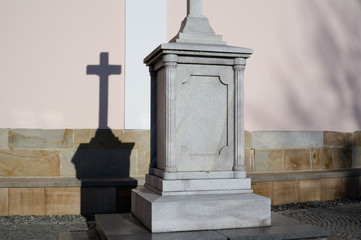 Obraz premium Religious sculpture of cross on solid stony pedestal. Detail of architecture with deep shadow on the wall behind it