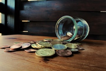coins faling from glass bottle on the wood table © maria