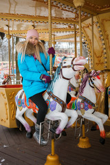 Young adorable blonde woman enjoys the winter holidays on the city park carousel. Winter active city lifestyle concept.