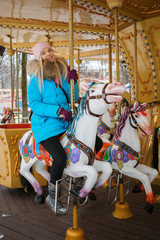 Young adorable blonde woman enjoys the winter holidays on the city park carousel. Winter active city lifestyle concept.