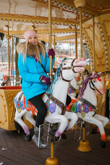 Fototapeta na wymiar Young adorable blonde woman enjoys the winter holidays on the city park carousel. Winter active city lifestyle concept.