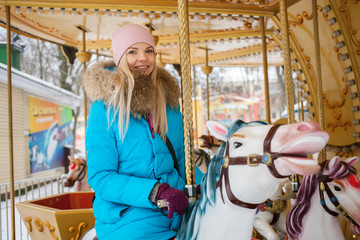 Obraz na płótnie Canvas Young adorable blonde woman enjoys the winter holidays on the city park carousel. Winter active city lifestyle concept.