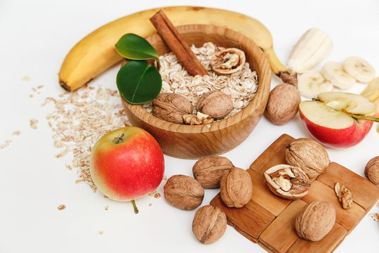 There are Banana,Apple,Orange with Walnuts in the Wooden Plate and Rolled Oats,Trivet,with Green Leaves,Healthy Fresh Organic Food on the White Background
