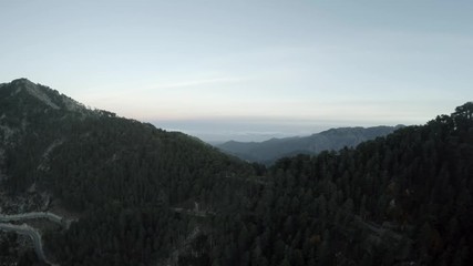 Aerial flying over mountain landscape at dusk showing mountain road below in background rest of mountain landscape end of day almost night flight and blue of sky just yet visible dark forest below 4k