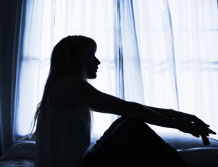 Silhouette of woman sitting in bed by window