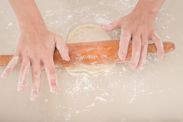 female hands rolling raw dough on white table