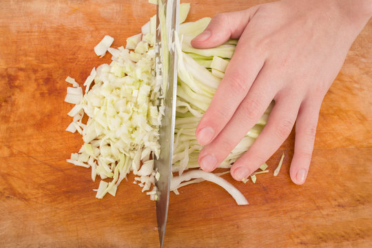 female hands slicing cabbage on wooden board