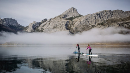 A group of people paddle surfing on a lake with fog and mountains