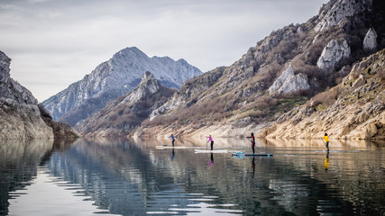 Un grupo de personas practica Paddle Surf en un lago con paisaje de montaña