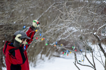 Man Putting up Christmas Holiday Lights in Snow Covered Trees Outdoors