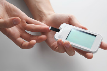 Woman checking blood sugar level by glucometer and test stripe at home