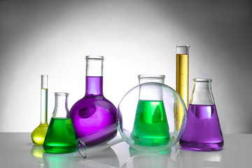 Chemical flasks and test-tube on color background
