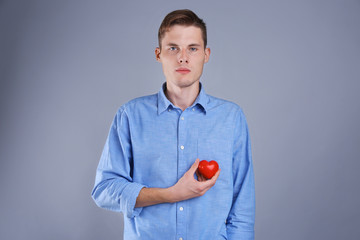 Handsome young man holding red heart on color background