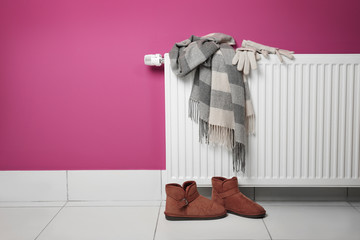 Warm clothes drying on heating radiator with shoes beside on the floor