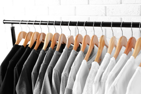 Black, grey and white t-shirts on hangers against brick wall, close up view