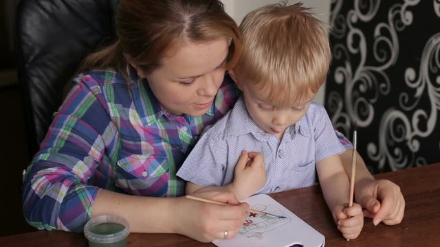 Young beautiful mother with son paint colors at home. Mom teaches son to paint colors.