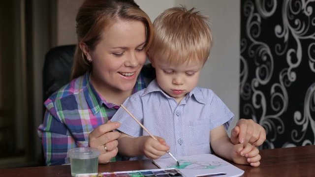Cute little boy painting with his mother at home. Adorable boy drawing with mother's help.