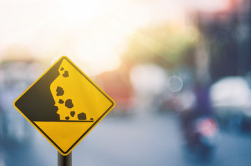 Falling stone warning traffic sign on blur road with colorful bokeh light abstract background.
