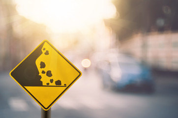 Falling stone warning traffic sign on blur road with colorful bokeh light abstract background.