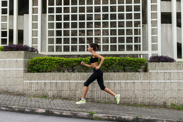 Side view of young female runner listening to music and jogging on sidewalk in town