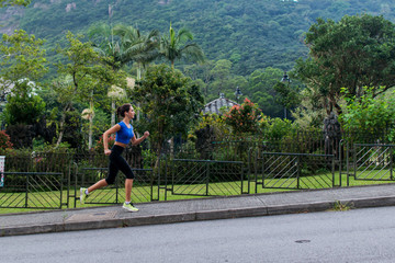 Athlete female runner doing cardio exercises in green mountainous area. Young woman jogging in nature landscape in summer