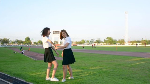 Two cute Asian Thai college student girl in university uniform walk in the scene holding hands playing with fun and joy in happy schoolgirl friendship and love relationship concept in HD