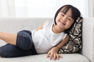 Naklejka premium Happy Asian Chinese little girl lying down on the sofa
