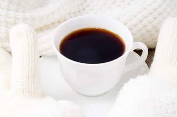 White cup with hot coffee and woolen mittens